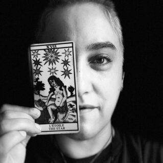 Person holding a tarot card with "The Star" illustration over their eye, in black and white.